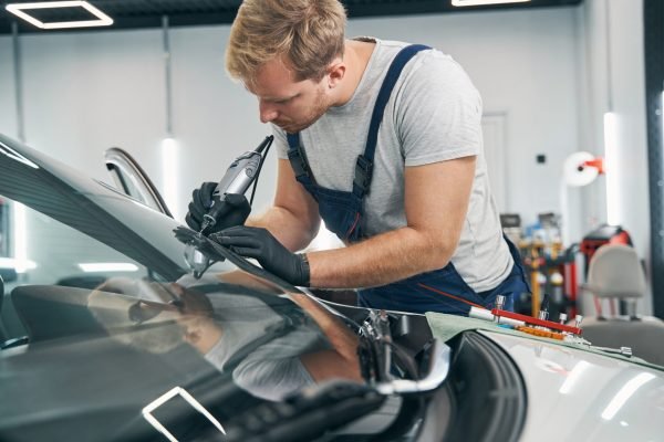 Car service technician checks crack on car windshield closeup Car service technician checks crack on car windshield closeup. Auto glass repair. Man in workshop